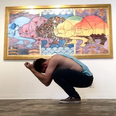 The artist, K Ryan Henisey, kneels before his painting, mimicking the pose of the figure in the art.