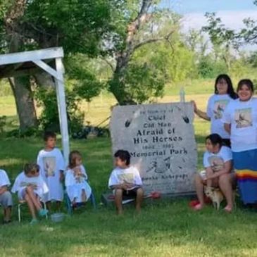 Group of children and adults by a memorial stone outdoors.