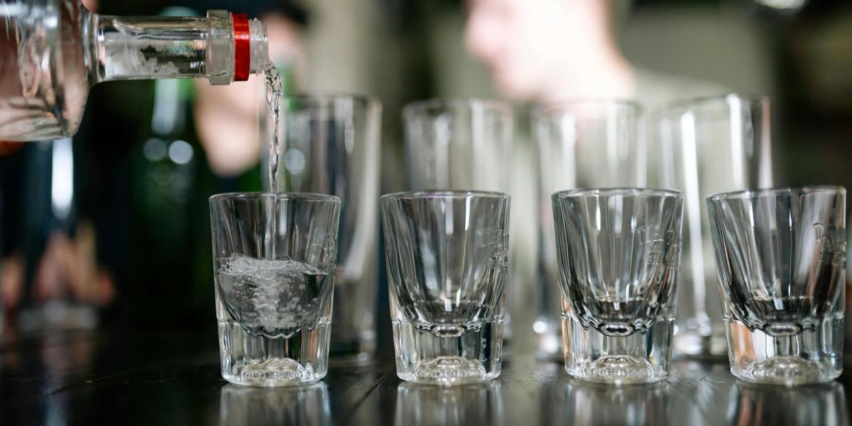 Liquor being poured into shot glasses lined up on a table.