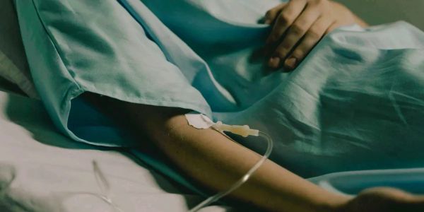Patient lying in bed with an IV line in the arm.