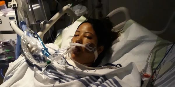 Person in hospital bed with breathing tubes.