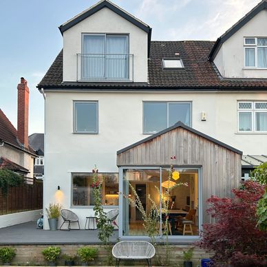 Modern white house with wooden patio extension and garden seating.