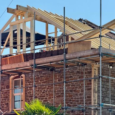 House under construction with scaffolding and new roof framing.