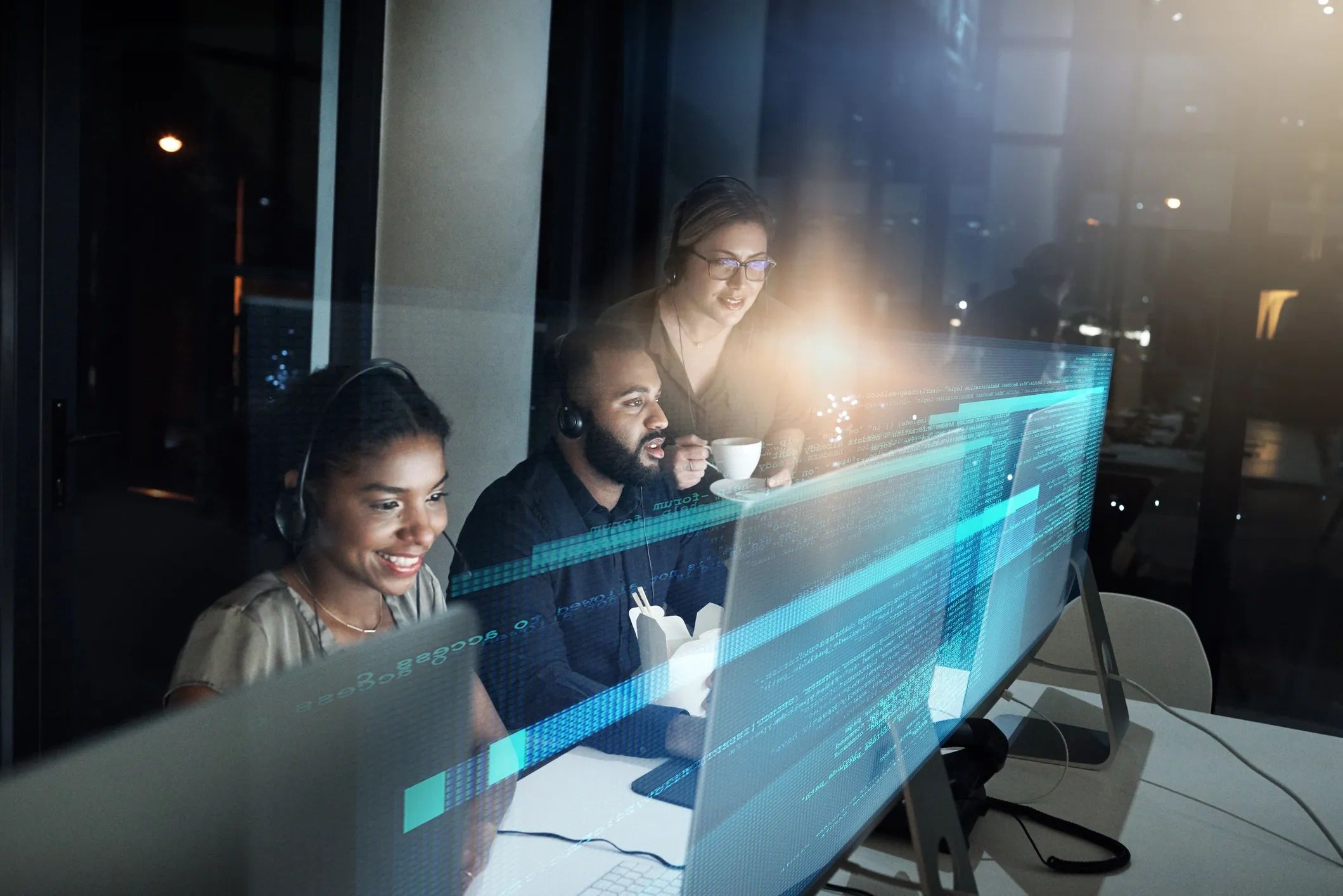 Three people working late in a tech office, focused on coding.