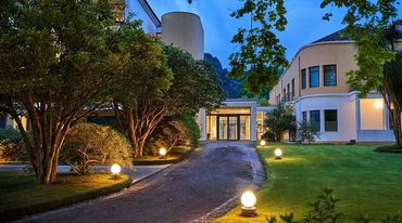 A well-lit pathway leading to a modern building surrounded by trees and greenery at dusk.