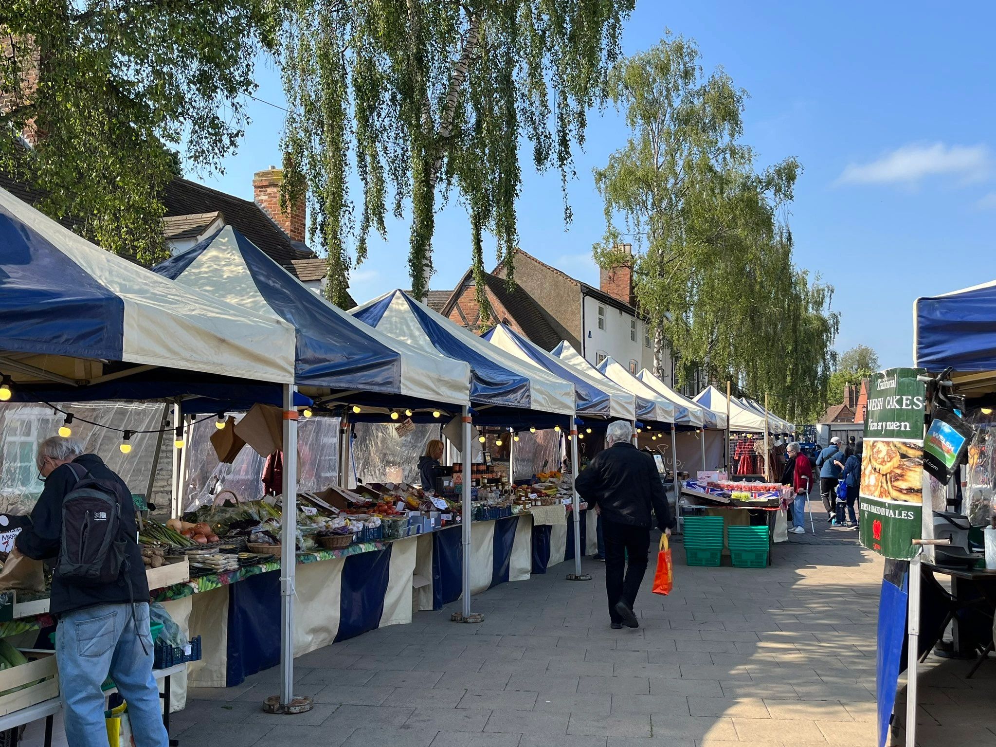 Outdoor market stalls with people shopping under blue skies.