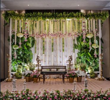 Elegant wedding stage with floral and greenery decorations, a wooden bench, and brass lamps.