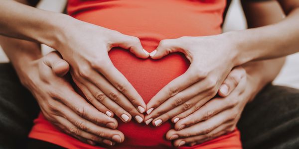Photo of a pregnant woman holding her hands in a heart formation over her stomach