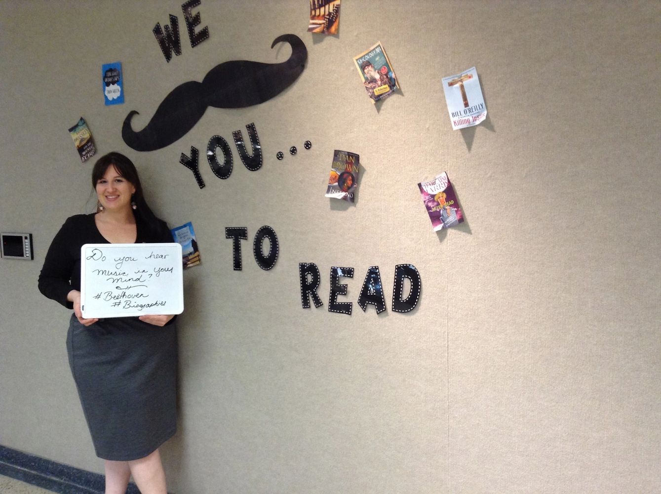 Ashley standing in front of a sign that says we mustache you to read.