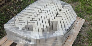 Stack of L-shaped concrete blocks wrapped in plastic on a wooden pallet.