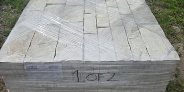 Stacked stone pavers wrapped on pallets outdoors.