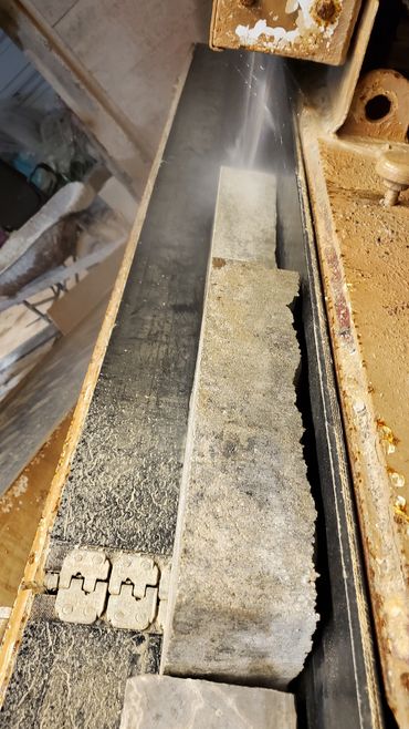 Stone slab being cut with water spray on a sanding machine.