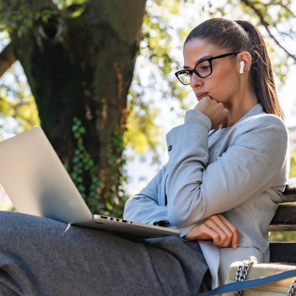 Woman wearing glasses and AirPods using laptop outdoors
