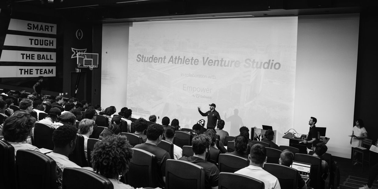 A speaker addressing an audience in a lecture hall with a presentation titled 'Student Athlete Venture Studio.'