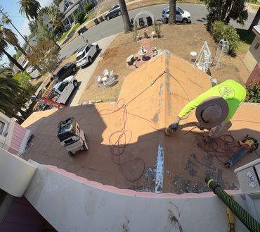 Worker in green shirt using power tools on a rooftop in a sunny neighborhood.