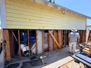 A worker stands in front of a partially demolished yellow house exterior.