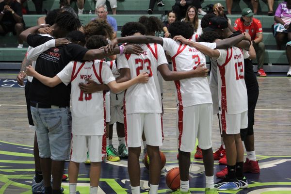 Youth basketball team huddles together on court in white and red uniforms.