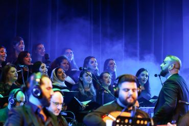 A choir and musicians performing on stage with blue lighting and smoke effects.