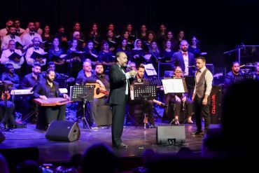 Toni Bayeh on stage with an orchestra and choir behind him.