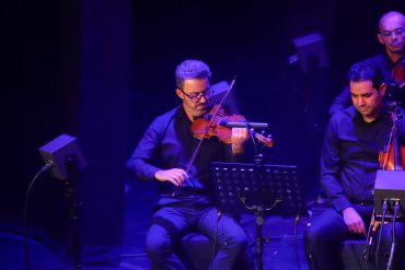 Violinists performing on stage under blue lights.
