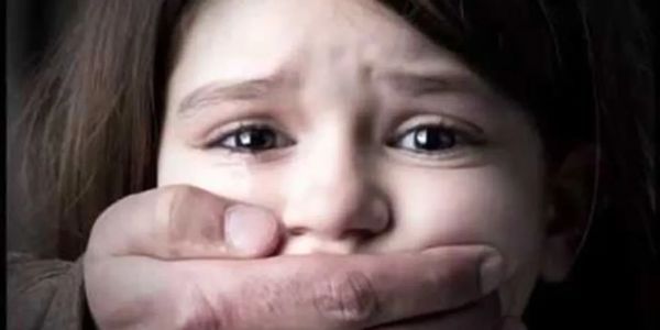A child with a hand covering her mouth, looking scared.