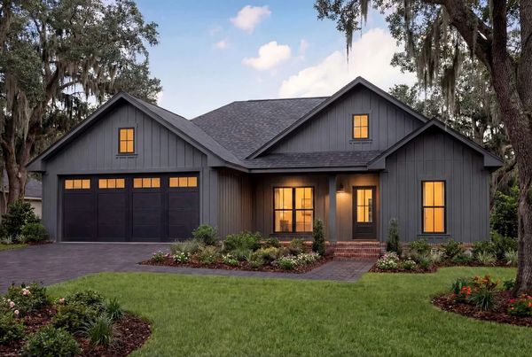 Modern gray house with warm lit windows and a manicured lawn at dusk.