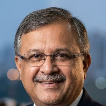 Smiling middle-aged man wearing glasses against a blurred cityscape background.