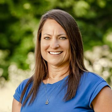 Smiling woman with brown hair in a blue shirt outdoors.