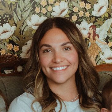 Smiling woman with wavy hair in front of floral wallpaper.