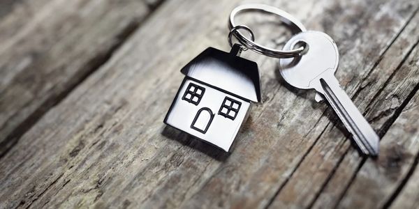 Key with house-shaped keychain on wooden surface.