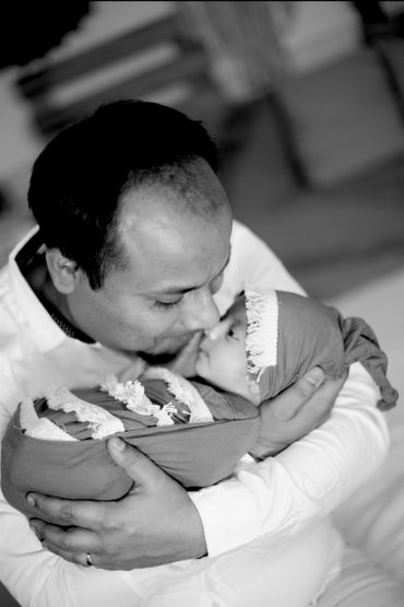 A father lovingly kisses his baby wrapped in a blanket and hat.