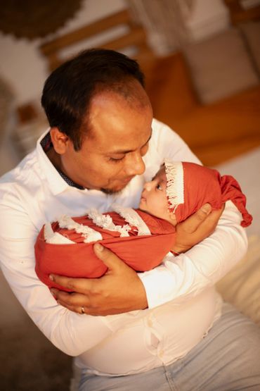 A father lovingly holding his newborn baby wrapped in a red blanket and hat.