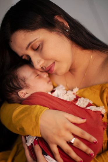 Mother lovingly cradles her sleeping baby wrapped in a red blanket.