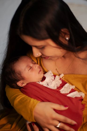 Mother tenderly cradling her sleeping baby wrapped in a red blanket.