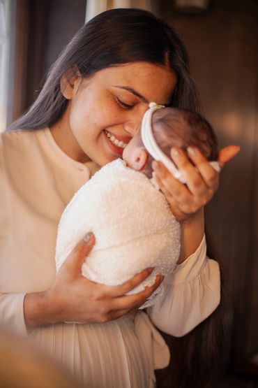 A mother lovingly holds and smiles at her newborn wrapped in a white blanket.