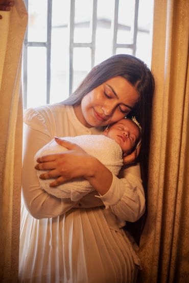 A woman tenderly holding a sleeping baby wrapped in a white blanket.