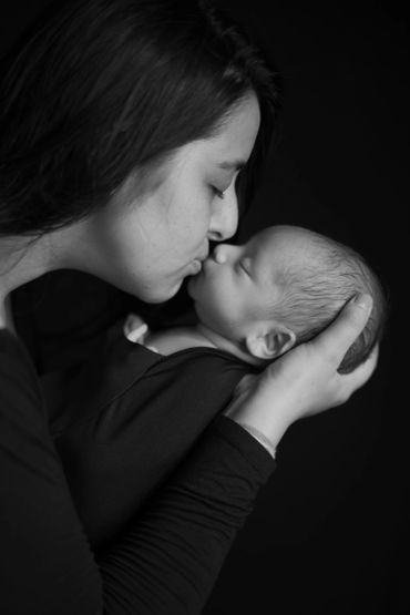 A mother gently kisses her sleeping newborn in a tender moment.