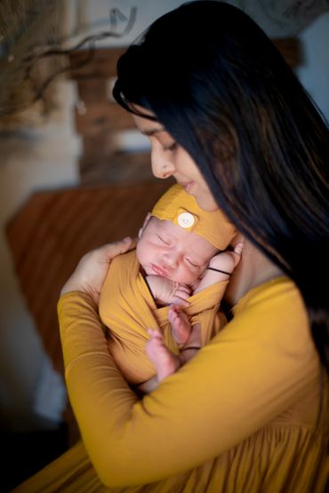 Mother tenderly holding her sleeping newborn wrapped in a yellow outfit.