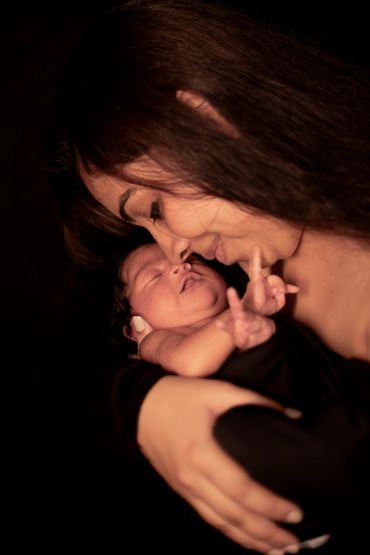 A mother lovingly holds and nuzzles her newborn baby wrapped in black fabric.