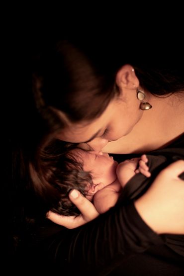 A mother tenderly cradles and kisses her newborn baby in a warm embrace.