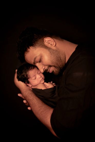 A tender moment of a father lovingly holding his sleeping newborn baby.