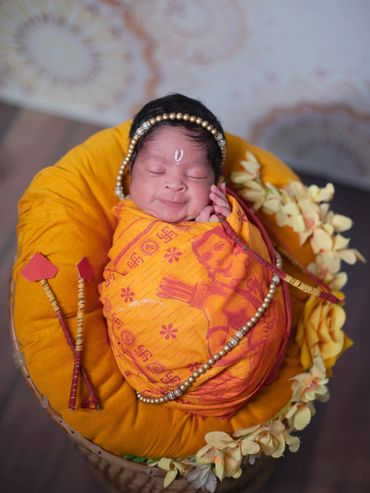 Newborn wrapped in traditional orange cloth with decorative beads and arrows, peacefully sleeping.