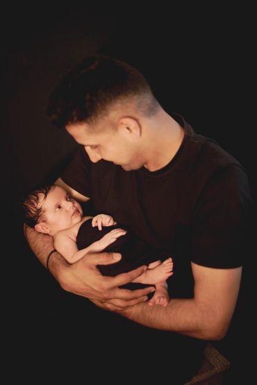 A father tenderly holding his newborn baby wrapped in black.