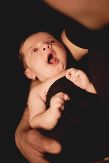Newborn baby yawning while being gently held.