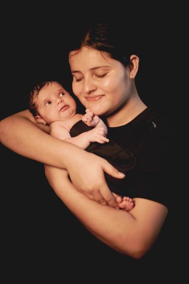 A woman lovingly cradles a baby against a dark background.