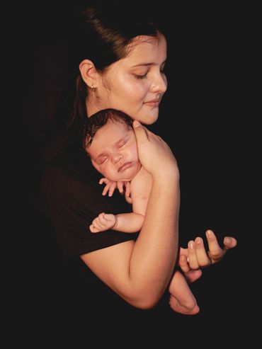 A mother lovingly holds her sleeping newborn against a dark background.