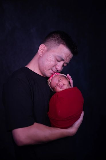 A father tenderly holds his swaddled newborn baby, both sharing a peaceful moment.