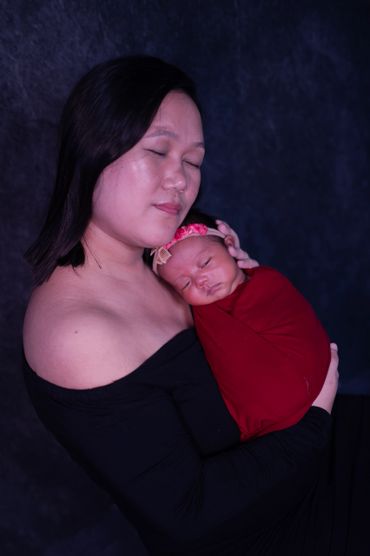 Mother gently cradling her sleeping newborn wrapped in red.