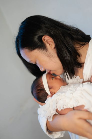 A mother tenderly kisses her newborn baby dressed in white.