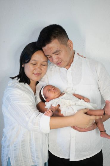 A loving couple holding their newborn baby dressed in white.